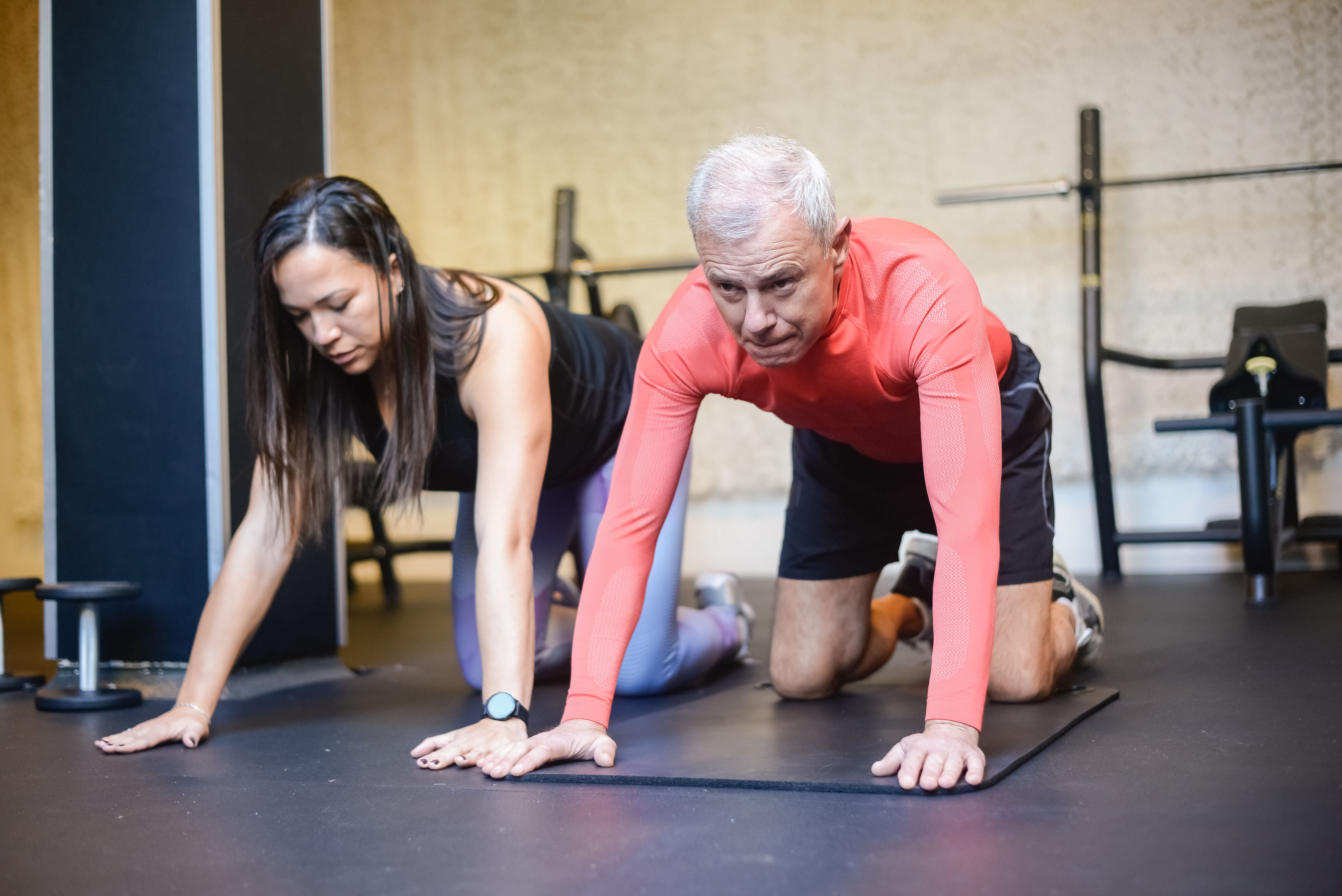 Coach accompagnant un adulte de plus de 50 ans lors d'un exercice de renforcement en salle.